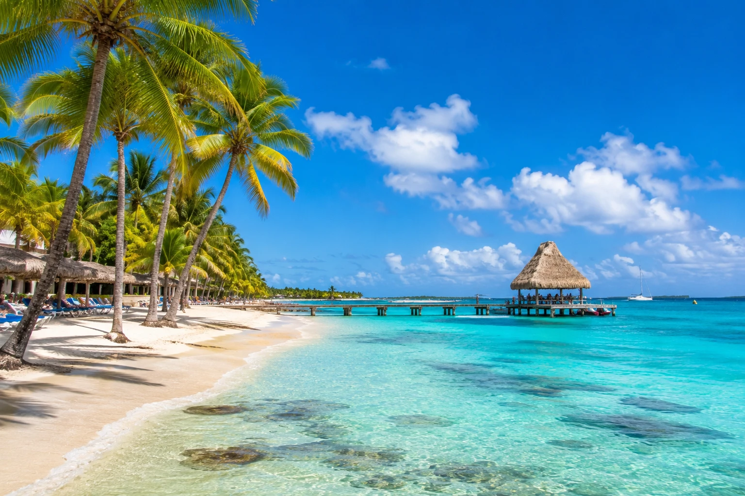Palm-lined white sand beach and thatched pier over turquoise water in Punta Cana, Dominican Republic